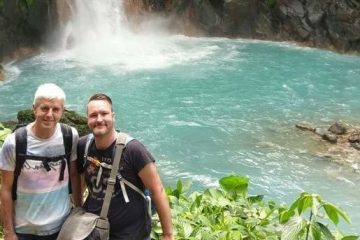 two men posing before a waterfall in a tropical forest in costa rica
